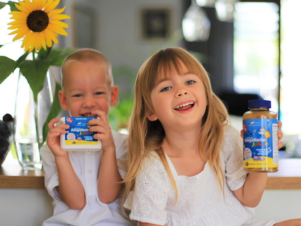Para uśmiechniętych dzieciaków pozuje z suplementem diety OmegaMarine Junior w jasnym, nowoczesnym wnętrzu.