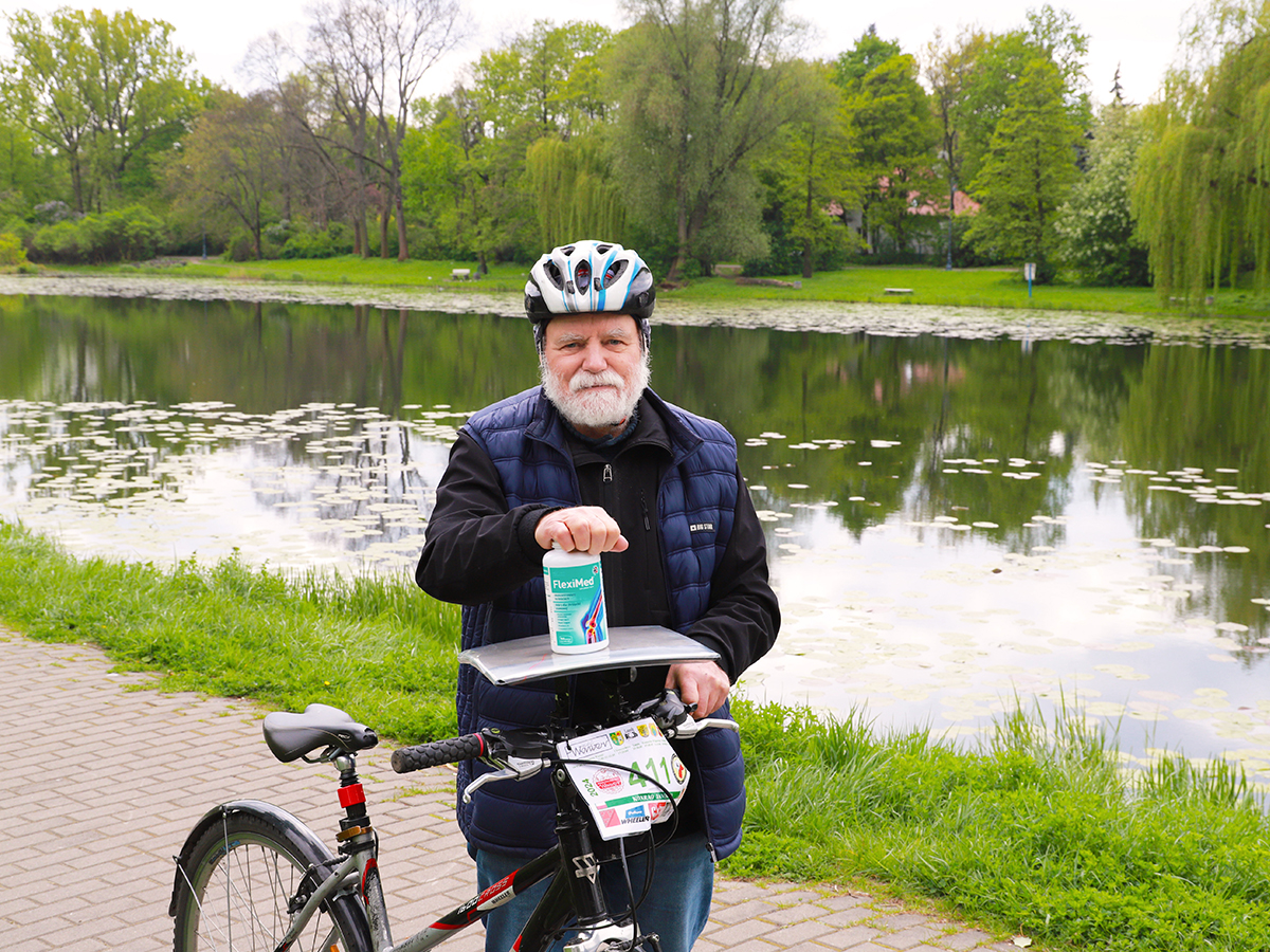 FlexiMed sprawia, że mogę więcej Pan Konrad pozuje z suplementem diety Fleximed Active na rowerze nad stawem.