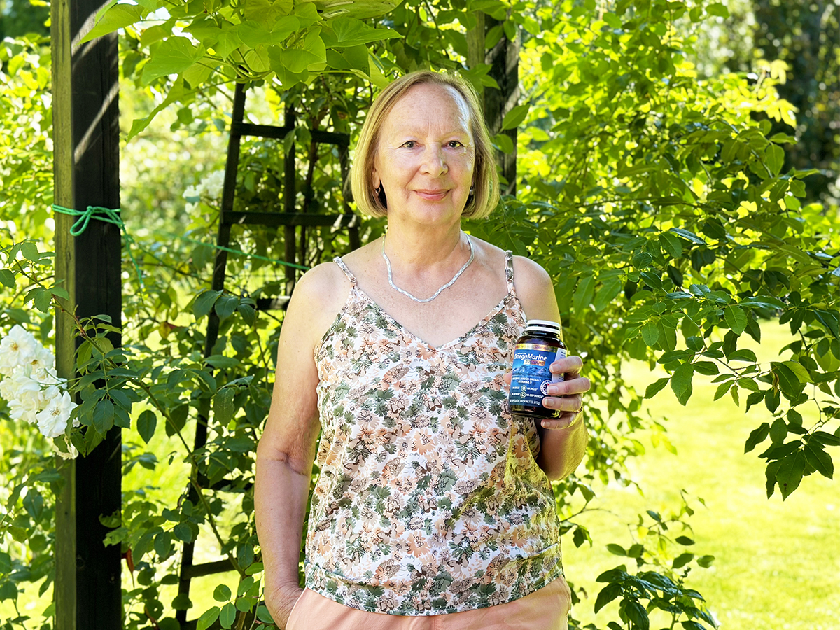OmegaMarine dba o moje serce Pani Krystyna pozuje na tle zieleni na swojej działce, trzymając suplement diety Omega Marine.
