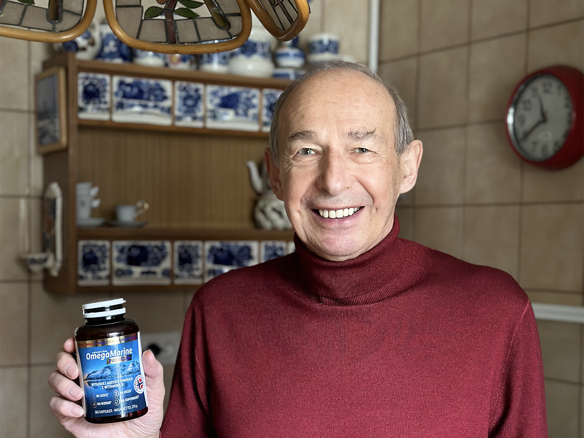 Pan Wojciech pozuje w czerwonym swetrze trzymając butelkę Omega Marine.